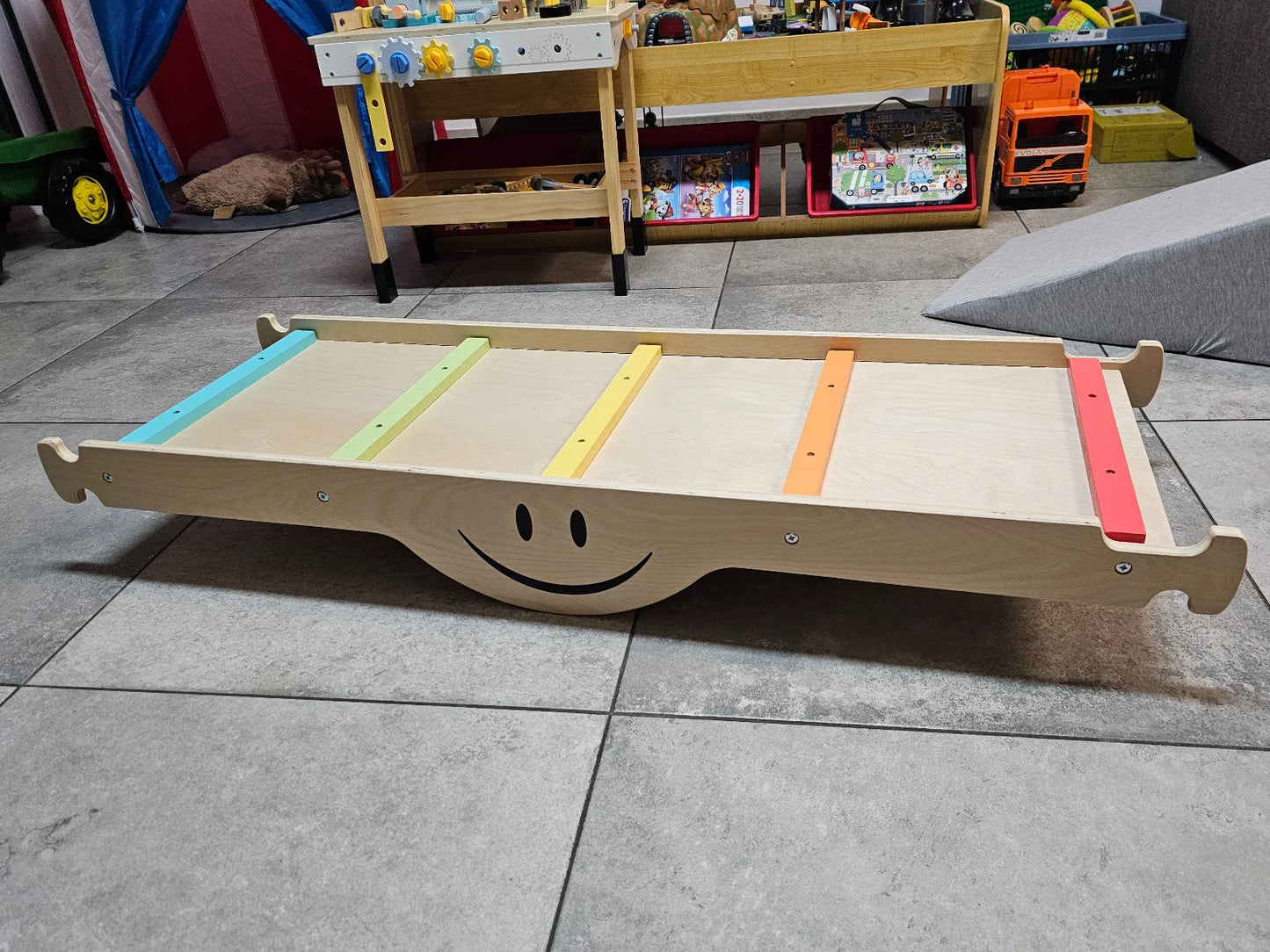 Balancierbrett aus Holz mit bunten Streifen und einem Smiley-Design.