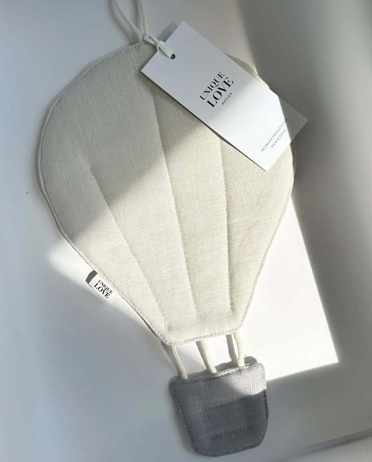 Heißluftballon-Dekoration aus weißem Stoff mit grauem Korb und angehängtem Produktanhänger.