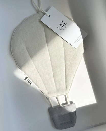 Heißluftballon-Dekoration aus weißem Stoff mit grauem Korb und angehängtem Produktanhänger.