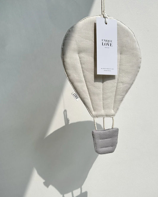 Heißluftballon-Dekoration aus weißem Stoff mit einem grauen Korb und einem Anhänger zum Aufhängen.