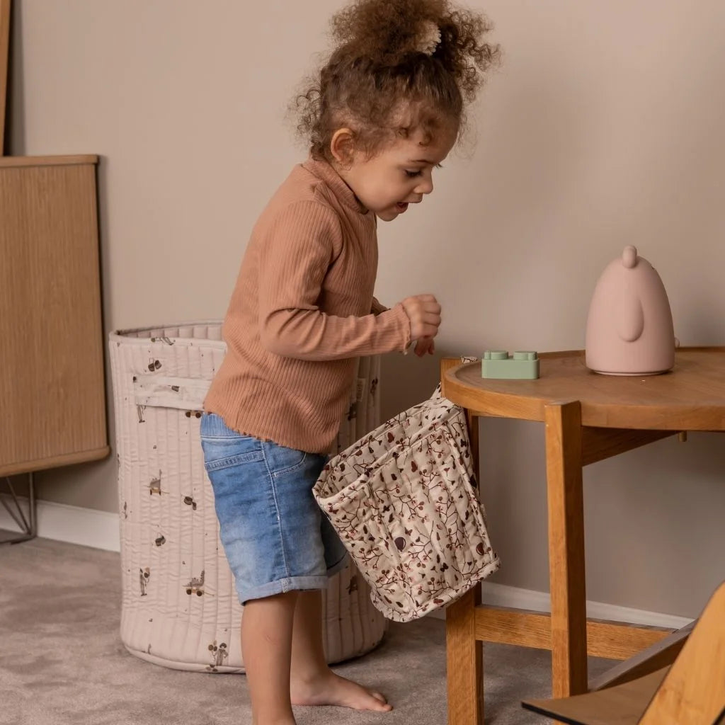 Ein Kind in einem braunen Pullover und Jeansshorts spielt mit einem gemusterten Korb.