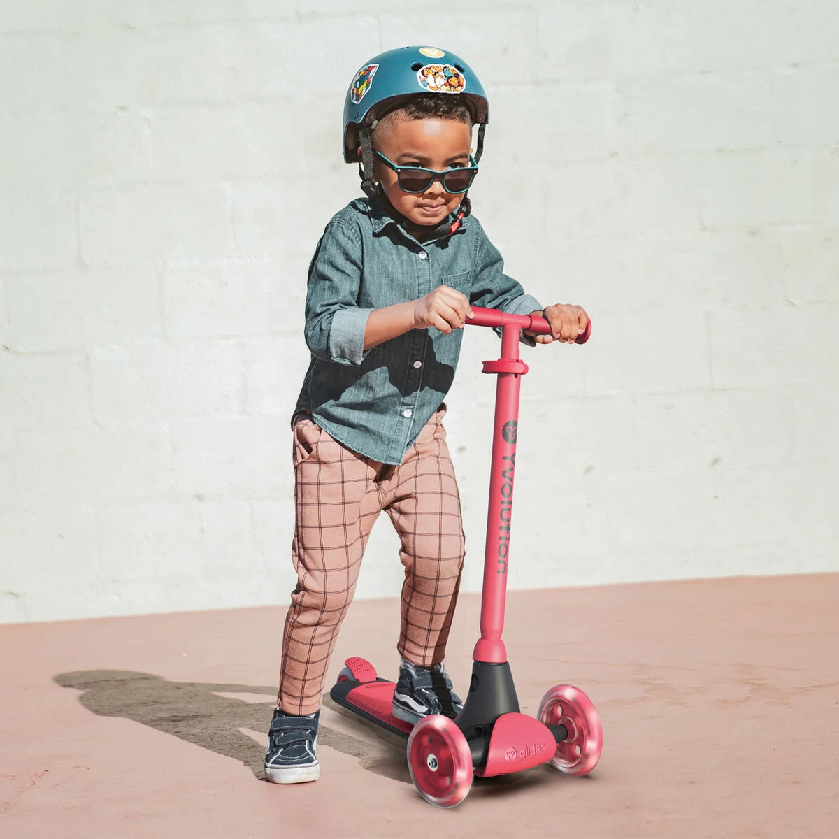 Rosa dreirädriger Tretroller mit einem jungen Fahrer, der einen Helm und eine Sonnenbrille trägt.