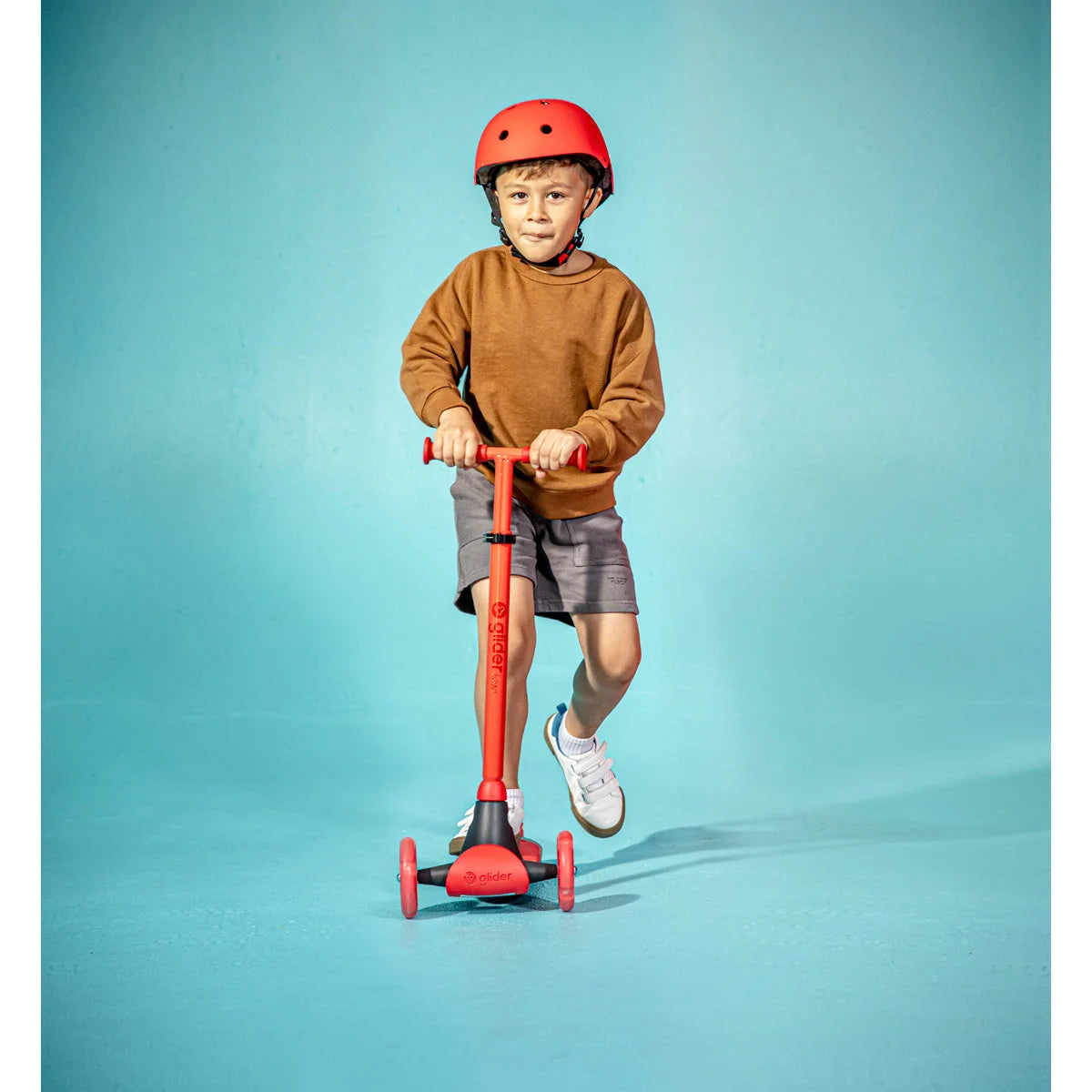 Ein Kind, das einen roten Helm trägt, steht auf einem roten dreirädrigen Motorroller.